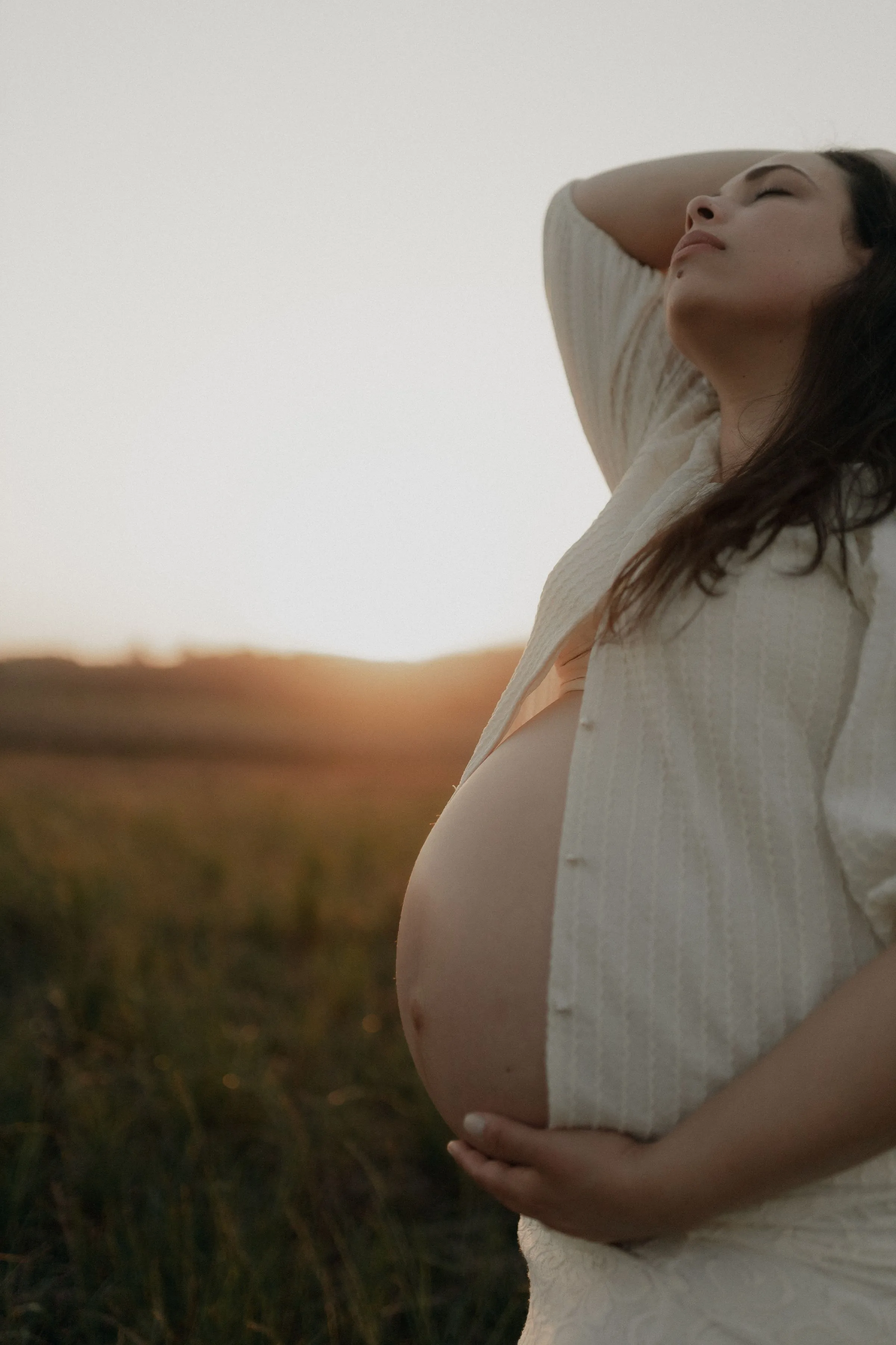 Une femme enceinte dans un champ, au soleil couchant